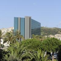a tall building with palm trees in front of a city at Tower Genova Airport - Hotel & Conference Center, Genoa
