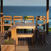 a wooden table and chairs on a deck with the ocean at Aloha 22, Ponta Mamoli