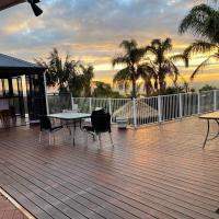 a deck with tables and chairs and palm trees at Lakeside Retreat, Perth