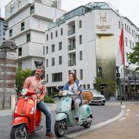 two people riding on scooters on a city street at HasHotel, Hasselt