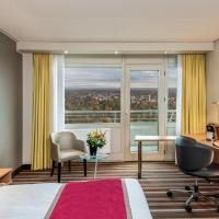 a hotel room with a bed and a desk and a window at Leonardo Royal Hotel Frankfurt