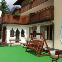 a house with a green lawn with two chairs on it at IHR Hotel Villa Emma, Canazei