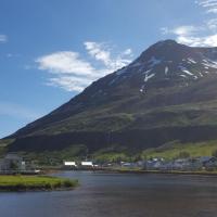 a mountain with a town in front of a river at Við Lónið Guesthouse, Seyðisfjörður