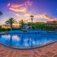 a pool at a resort with palm trees and a sunset at Lagomandra Hotel and Spa