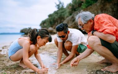 Three people on a beach collecting water and sand in a cup.